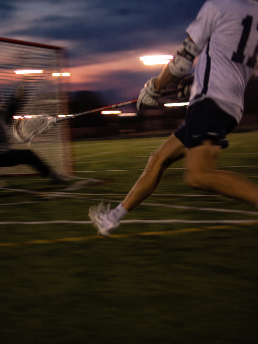 Lacrosse player driving toward the goal at dusk