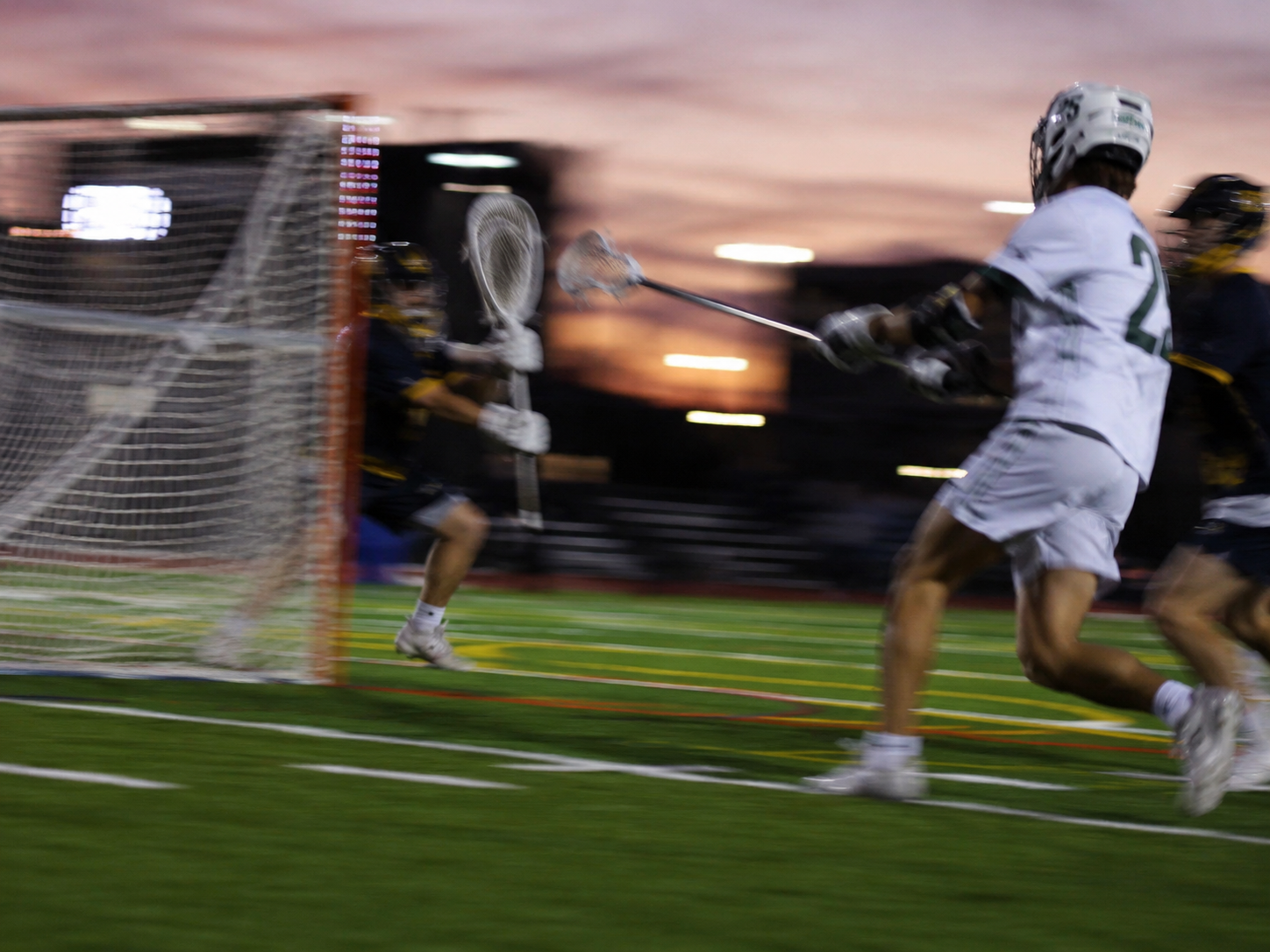 Lacrosse player driving toward the goal at dusk