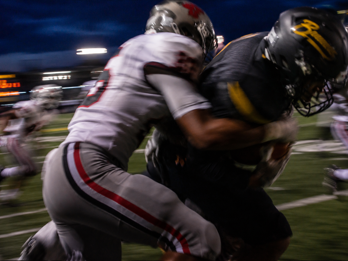 Two football players colliding under stadium lights