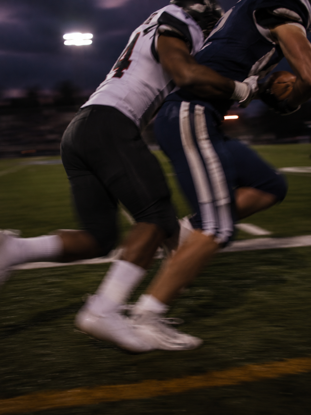 Two football players colliding under stadium lights